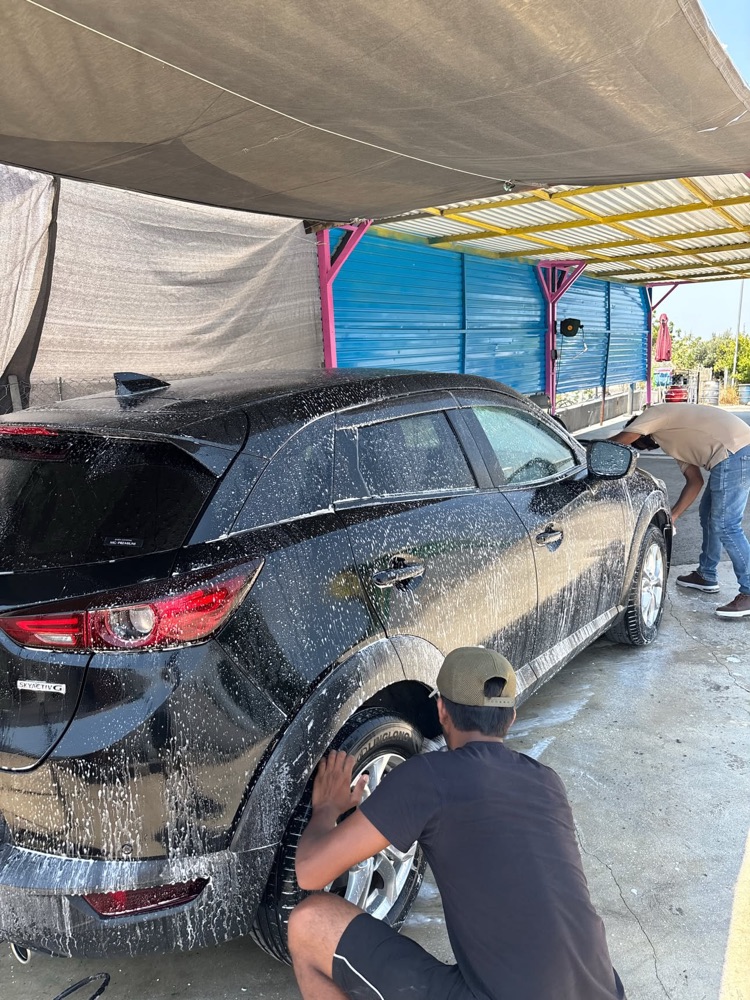 Two GlossLab staff hand washing a black hatchback, one scrubbing the wheel arch